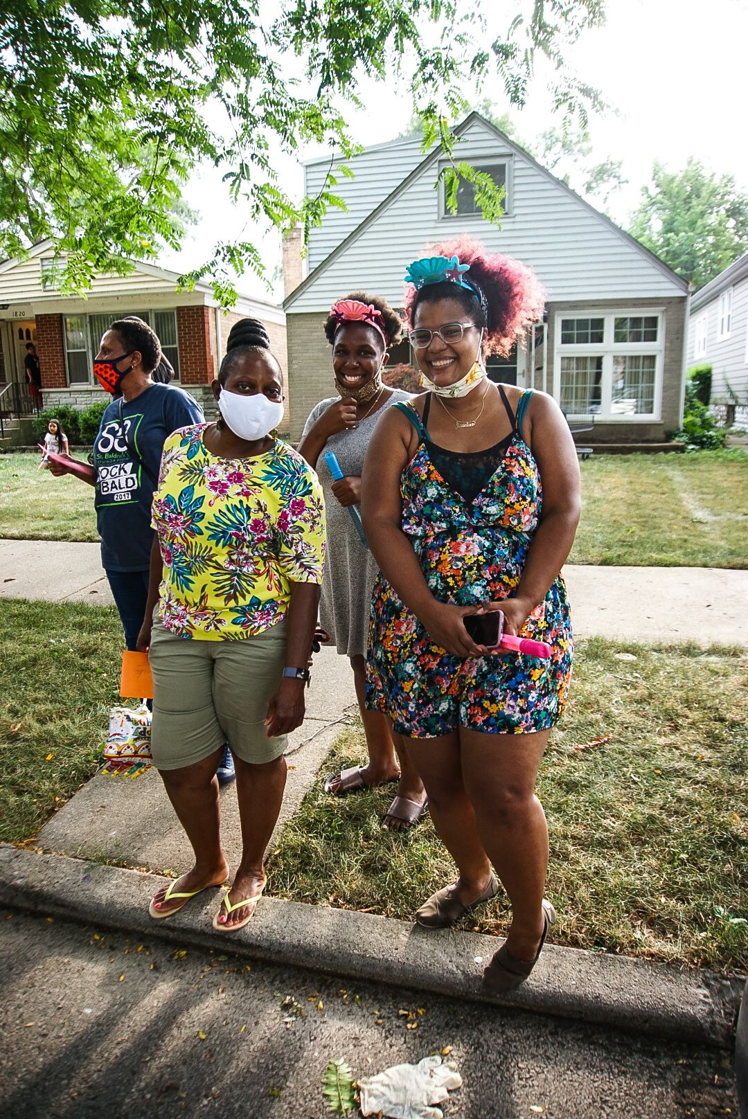 Four people in colorful summer outfits stand together on a suburban sidewalk.