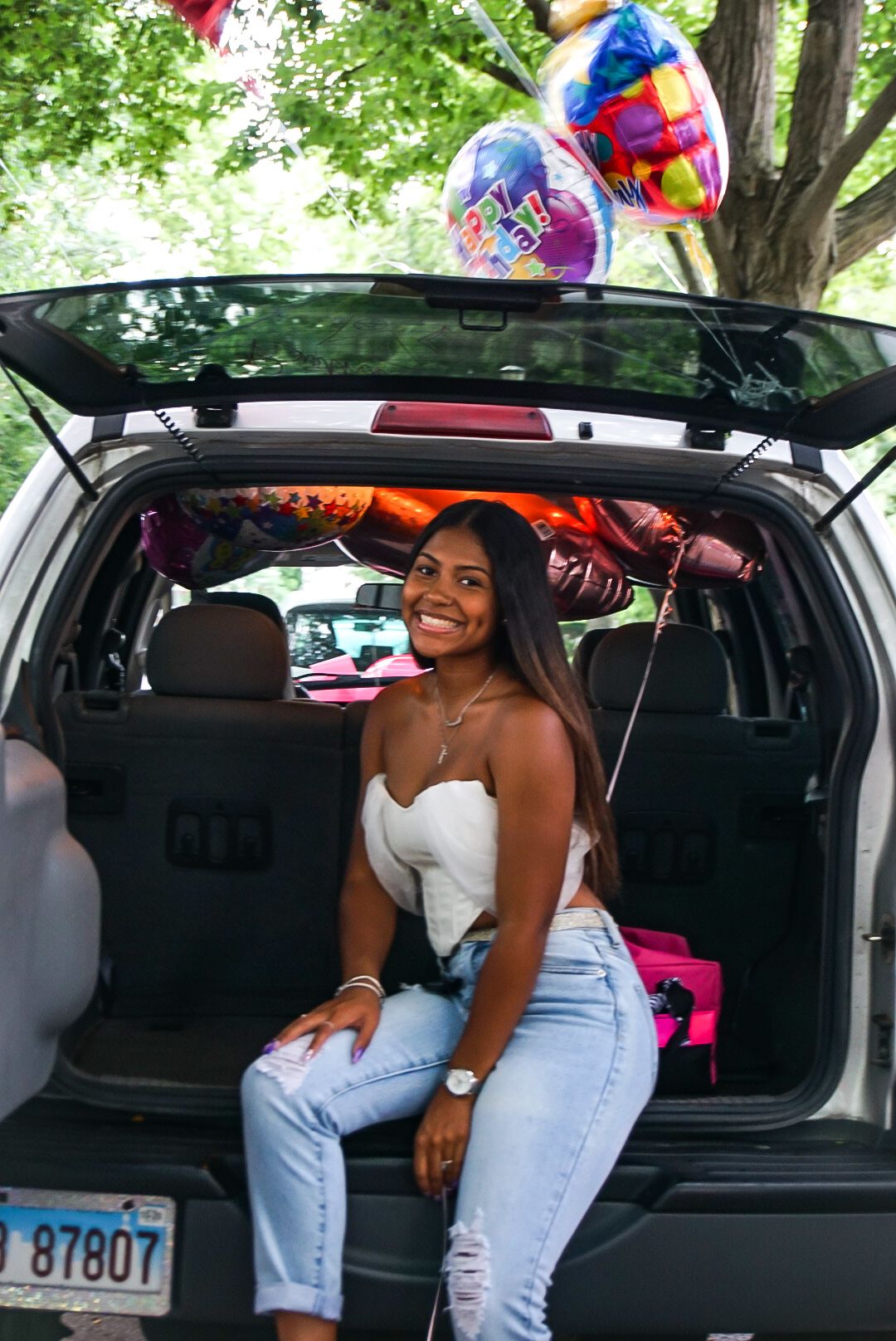 Someone in white sits in the trunk of an SUV decorated with celebration balloons.