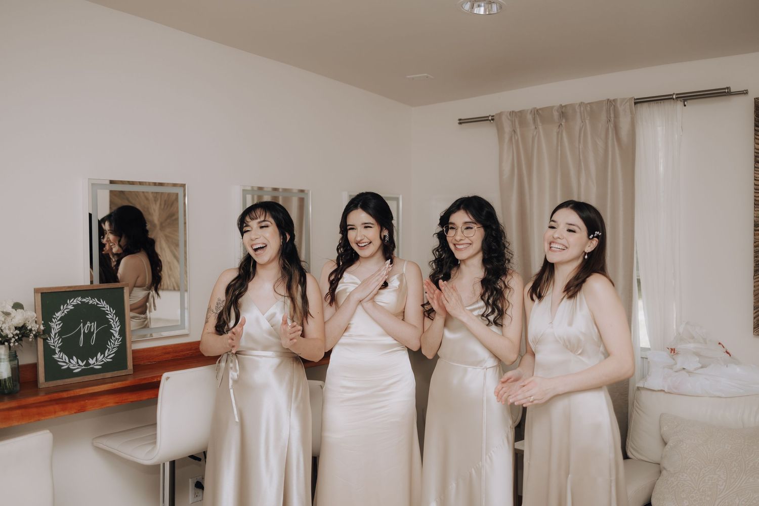 Wedding party in matching champagne dresses stands together in a bedroom.
