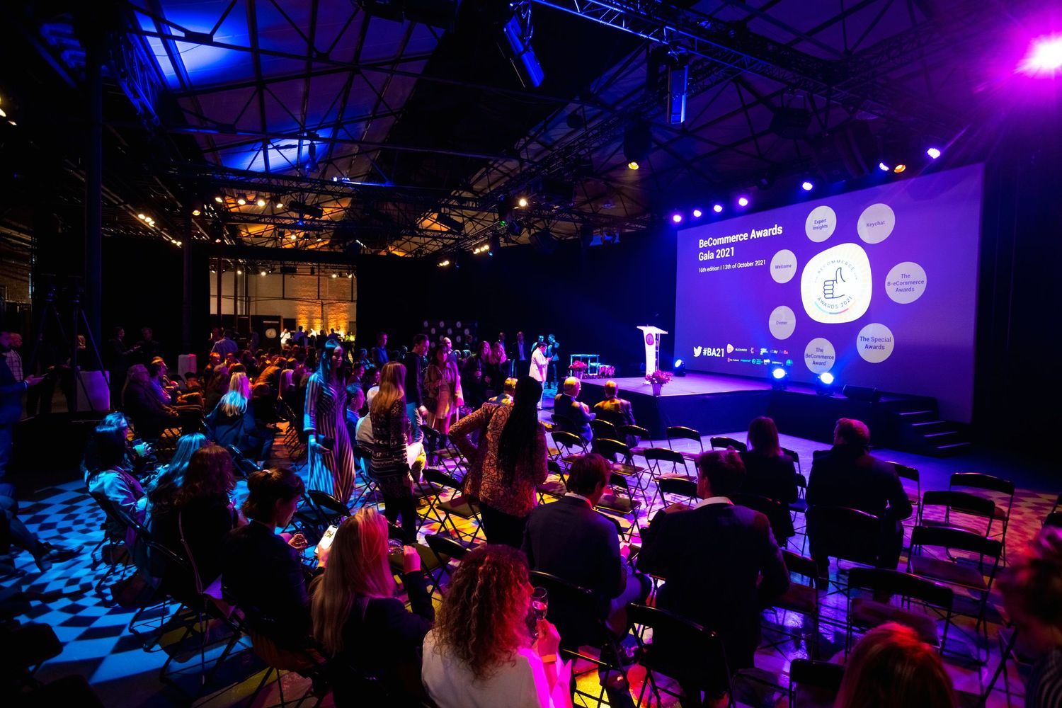 Crowd enjoying nightclub event with colorful lighting and projected visuals on screen.