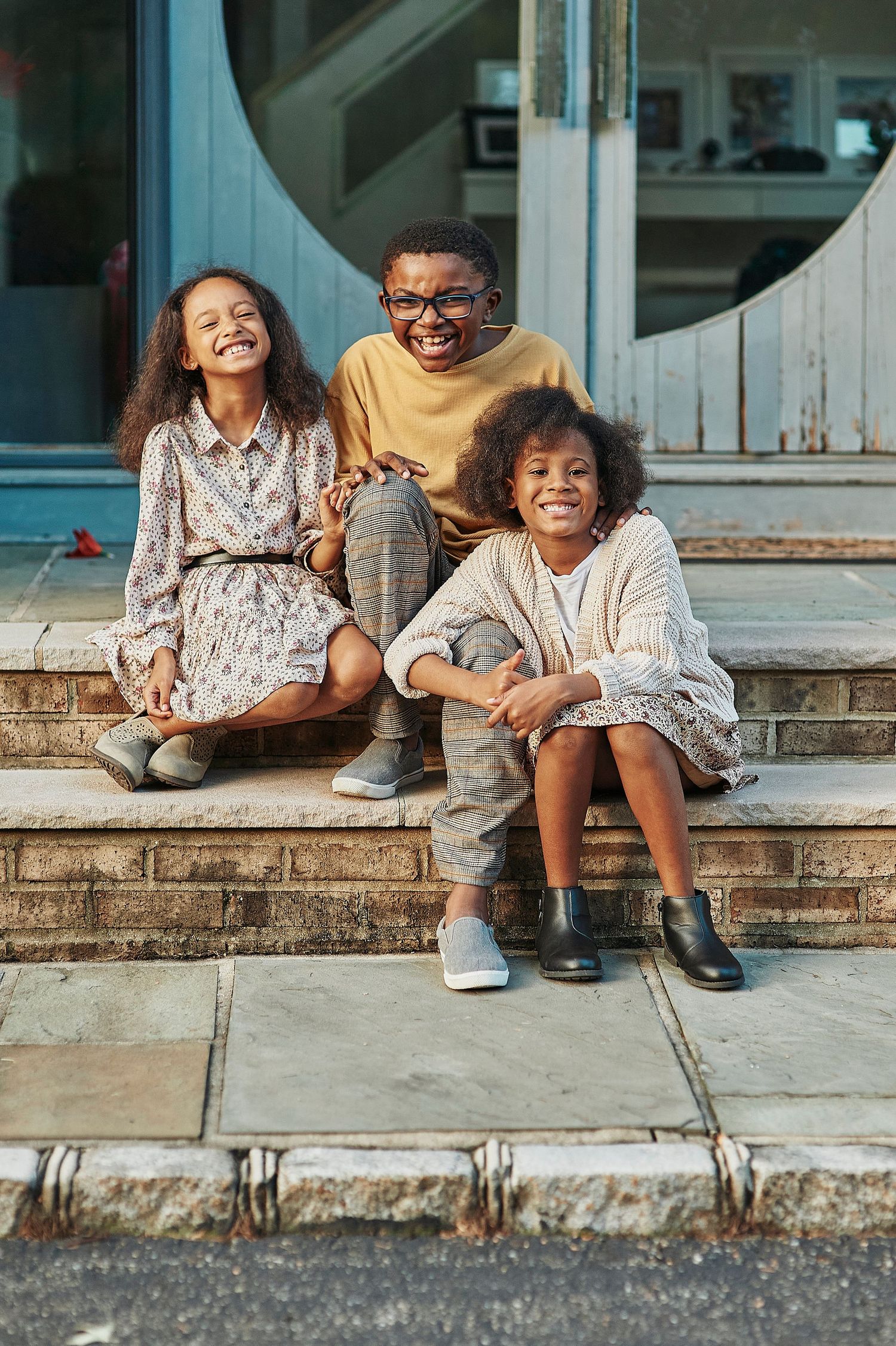 Three happy African American children sitting together on outdoor steps, smiling and laughing.