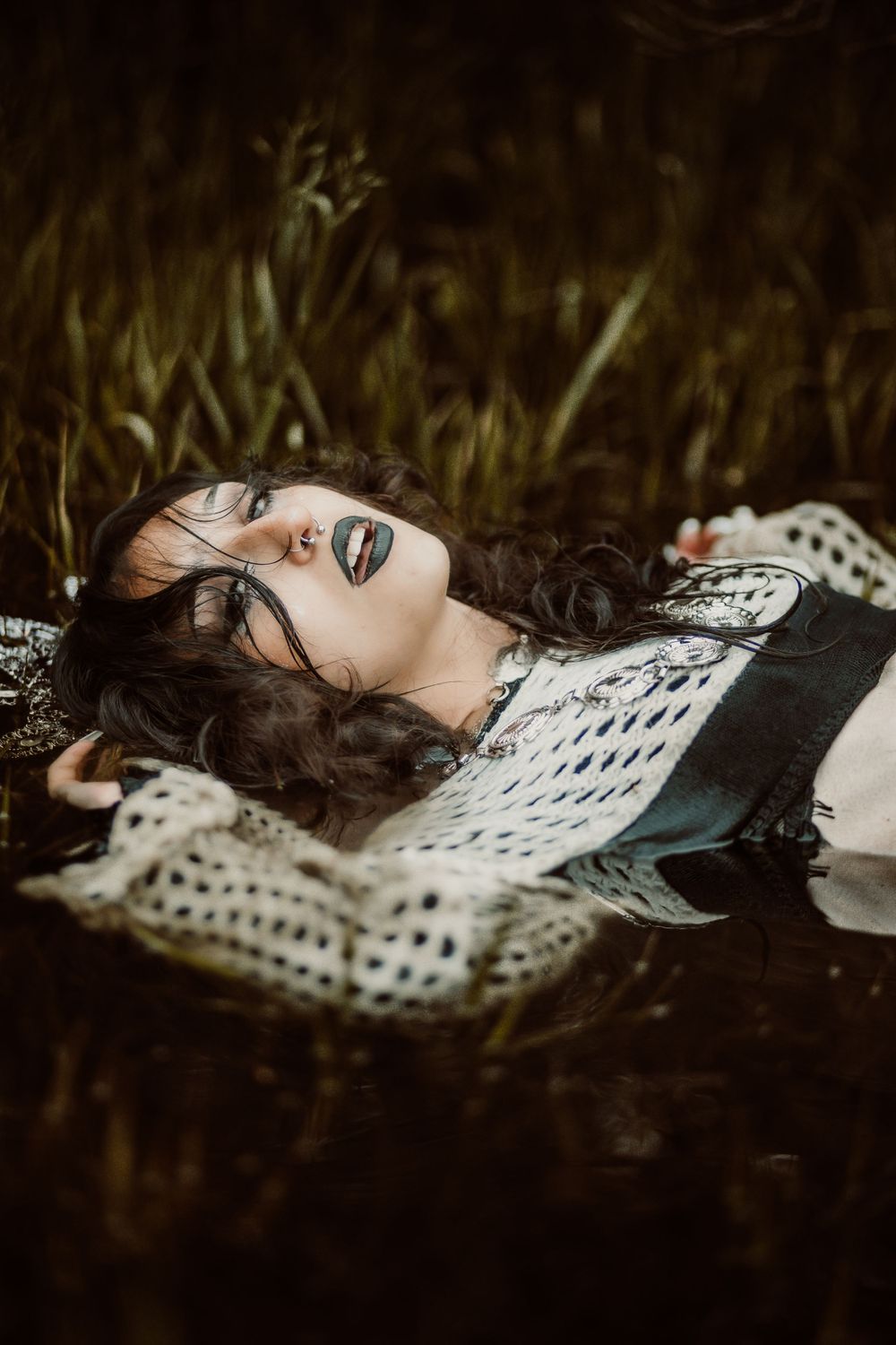 Artistic portrait of person in white crochet lying in dark grass.
