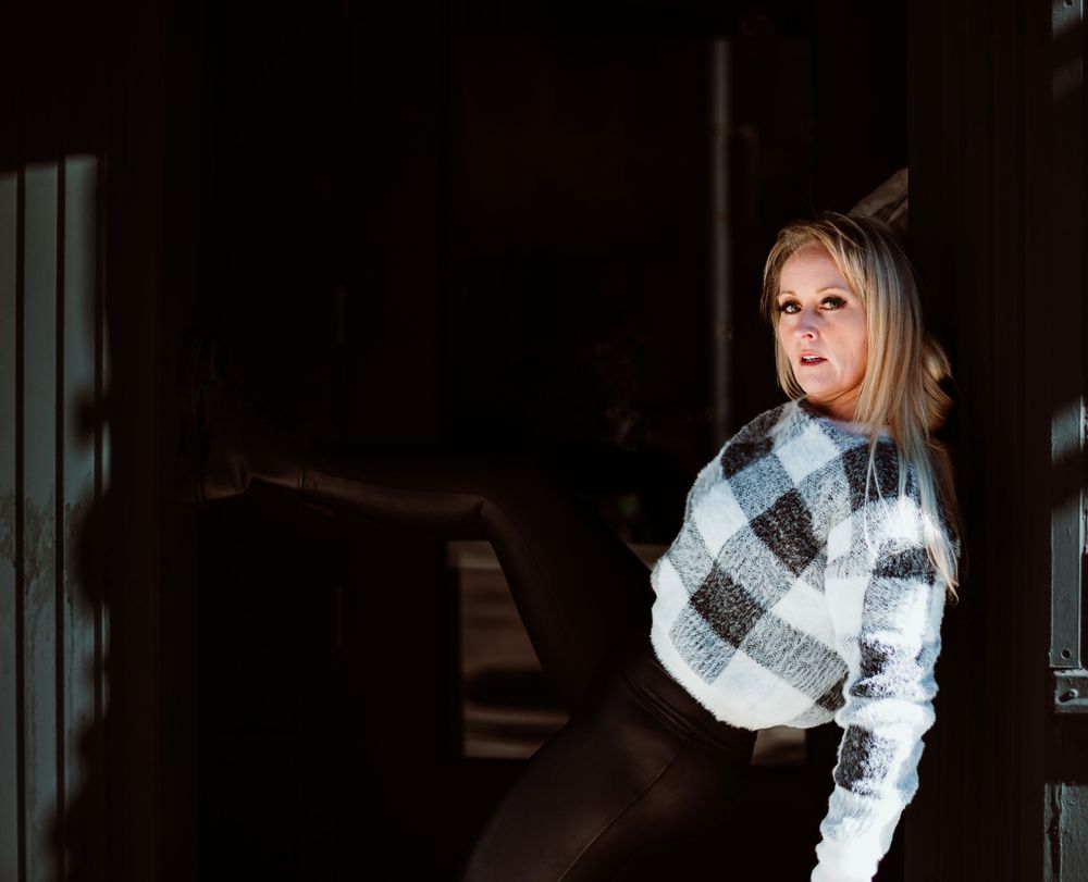 A person in a plaid sweater poses dramatically in moody lighting.