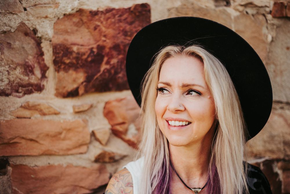 Portrait of someone in a black hat against a rustic stone wall background.