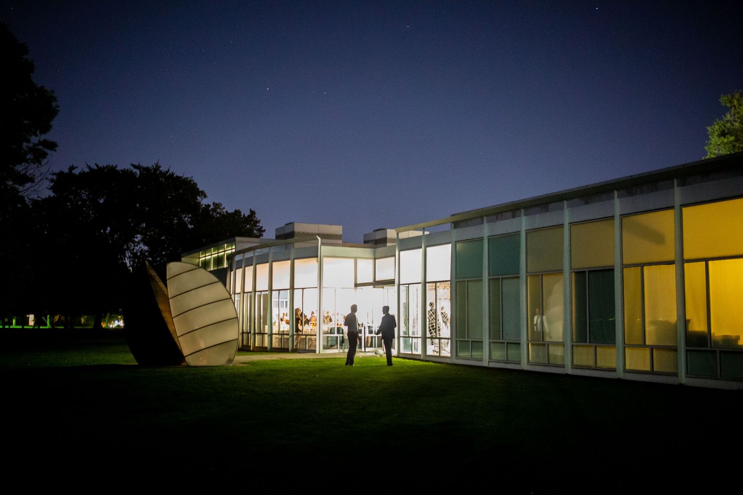 Modern glass building illuminated at night with colorful windows and architectural features.
