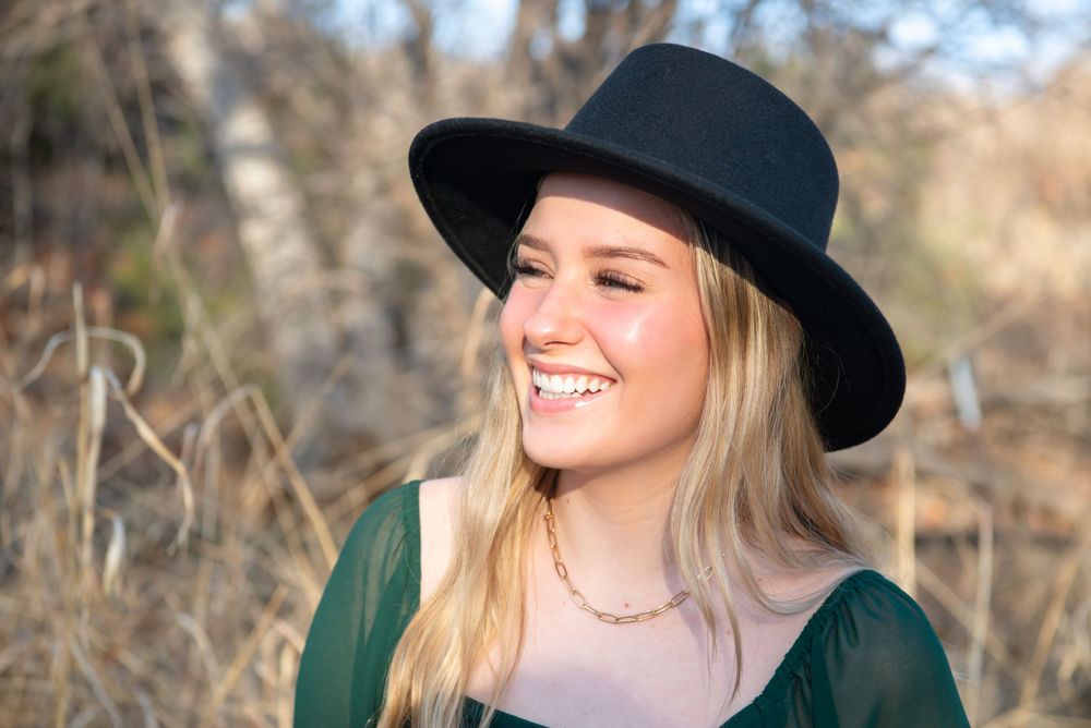 A joyful portrait of someone wearing a black hat and green top in a natural outdoor setting. Senior Portrait Photography Sedona Arizona