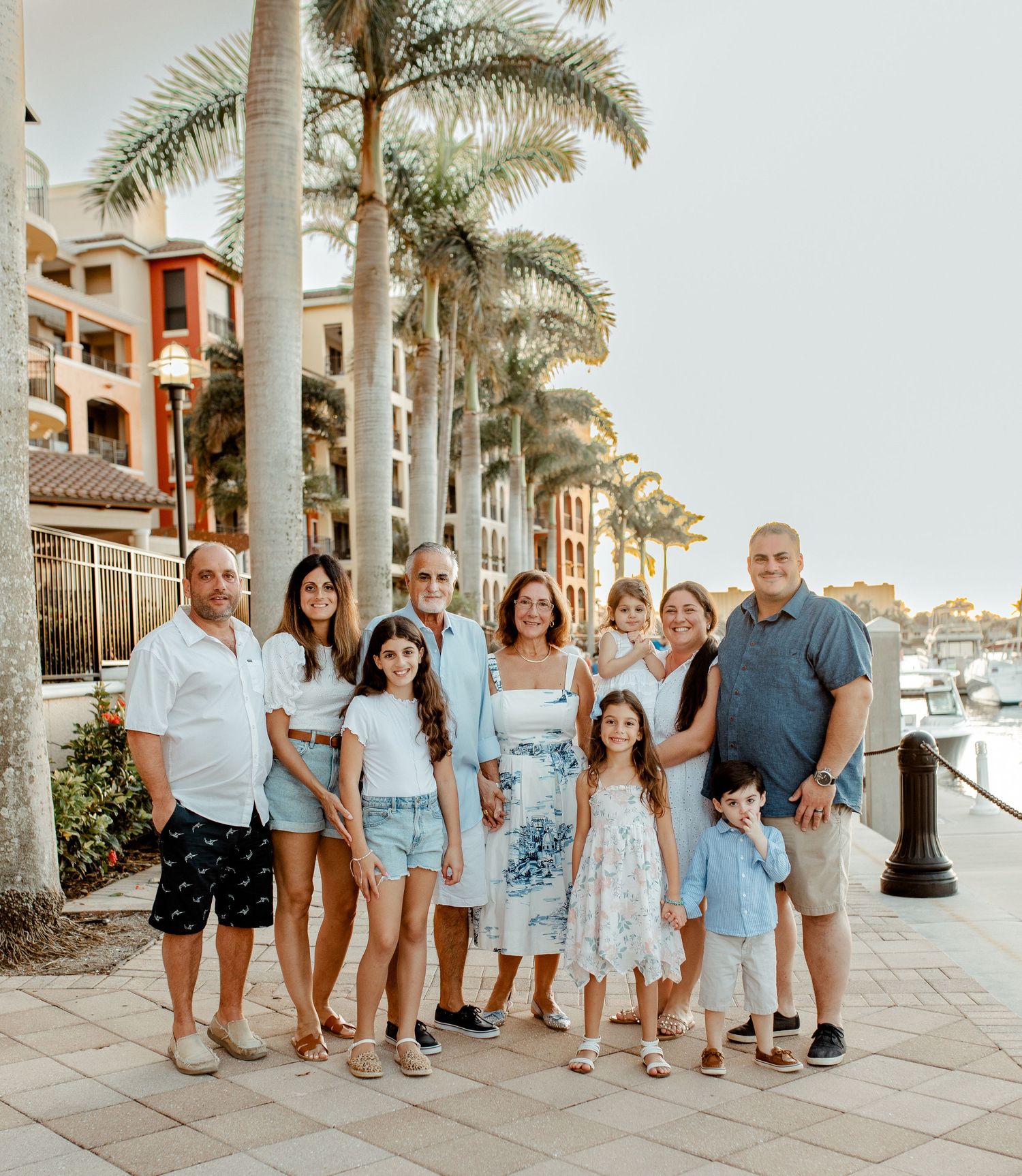Extended family group poses together on a palm-lined waterfront promenade.