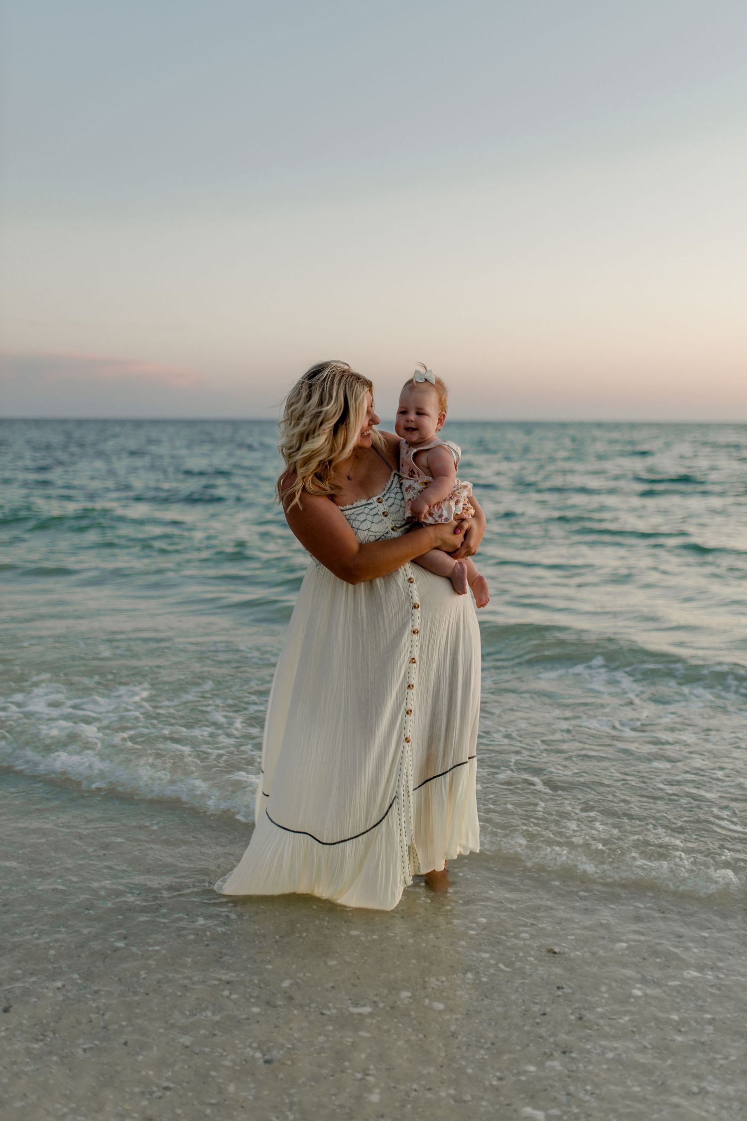 A touching moment between parent and child standing in the surf at dusk.