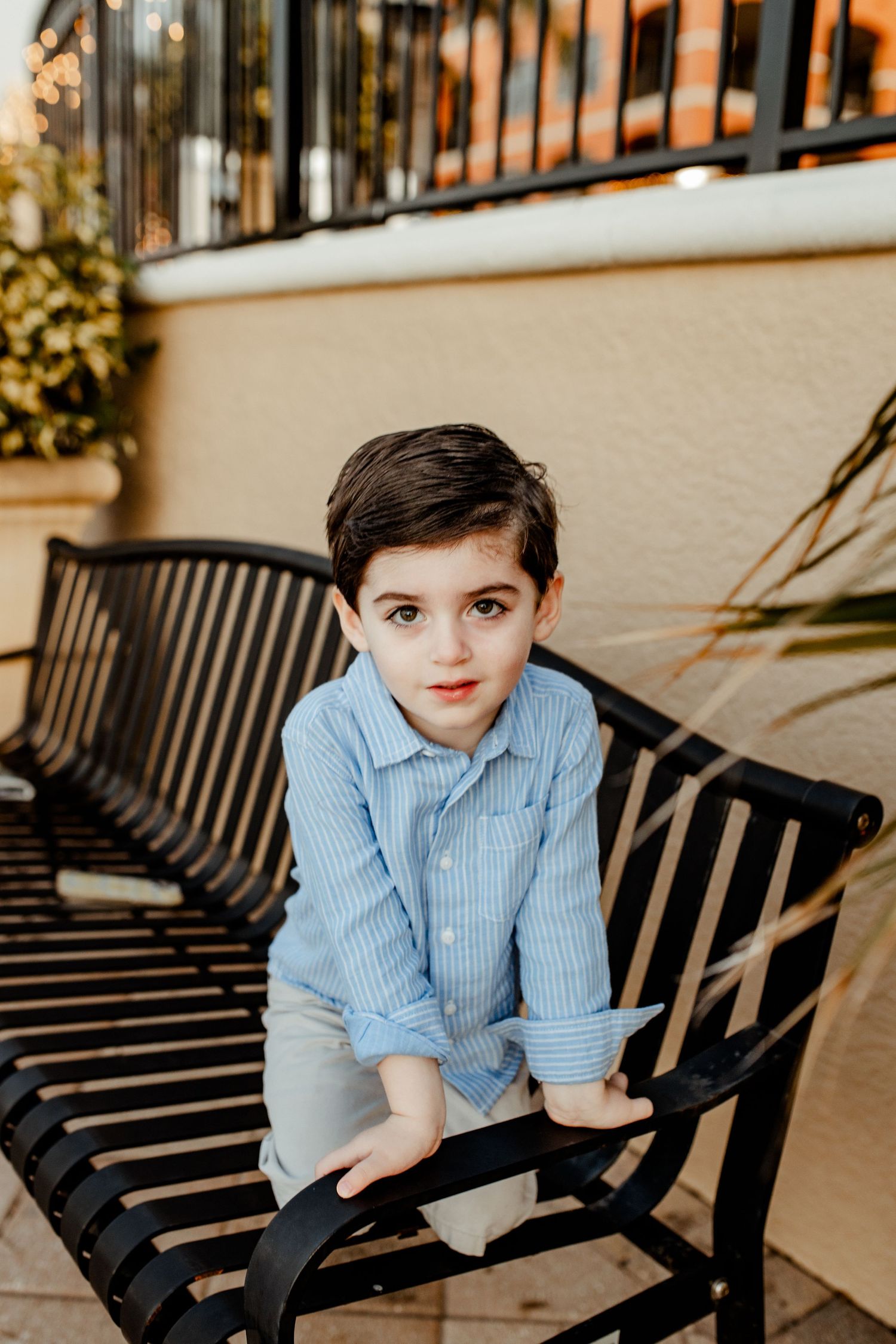 Young boy in blue striped shirt sits on black bench outdoors.