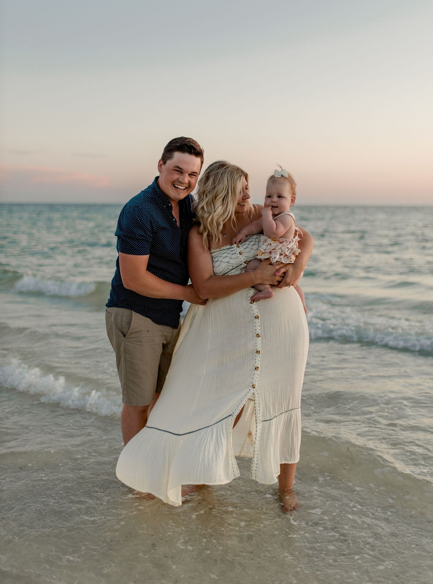 Family shares a tender moment at sunset on a beach with waves gently lapping at their feet.