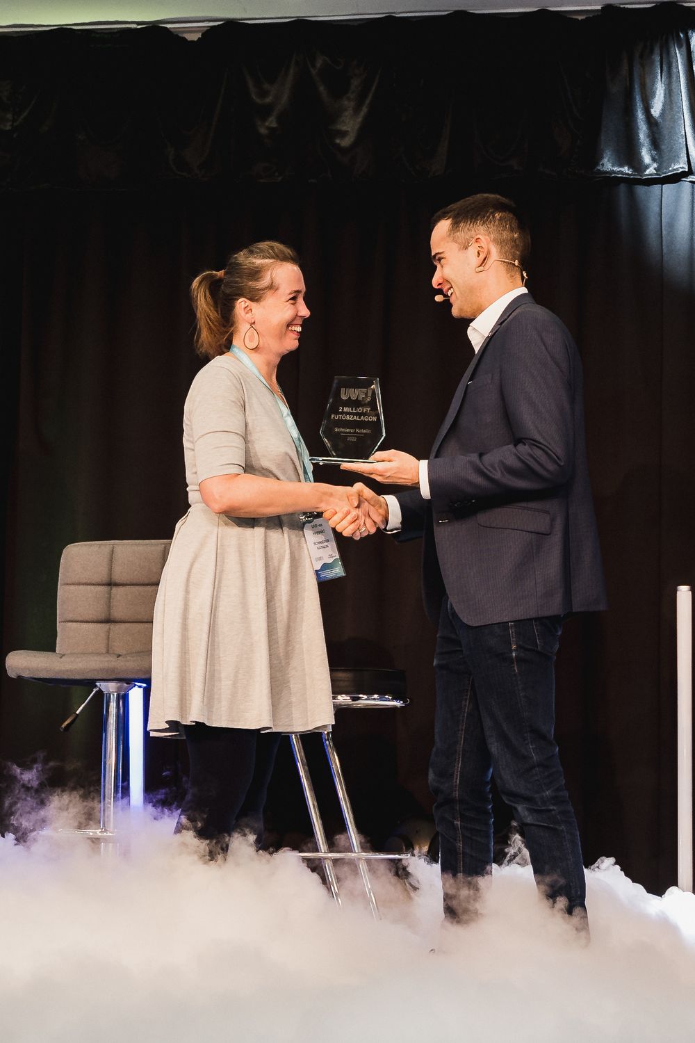 Award ceremony moment on stage with fog effects and dark curtain backdrop.