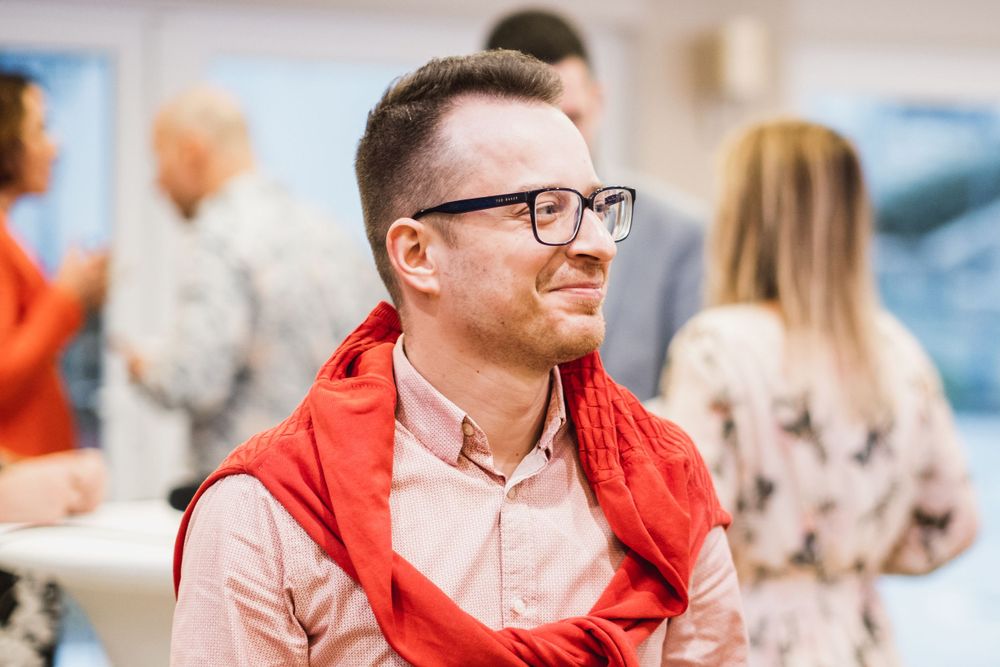 Participant in red jacket and glasses smiling during conference session.