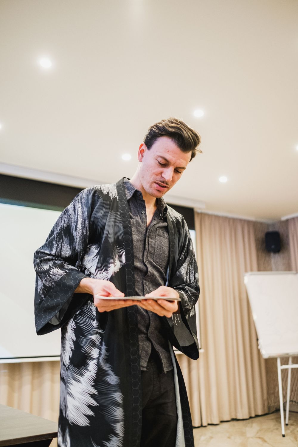 Speaker in stylish black patterned jacket reviewing notes during presentation.