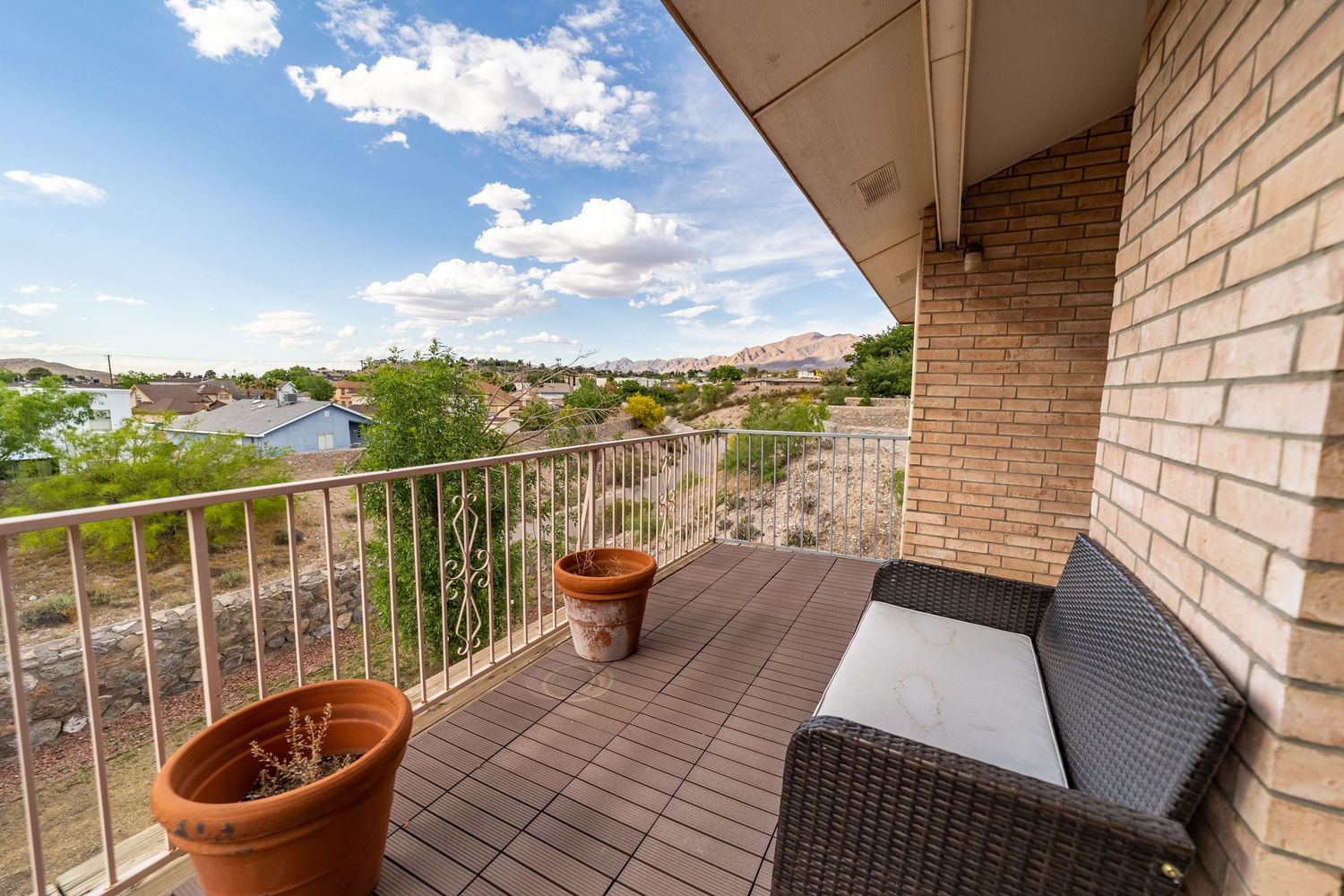 A modern balcony with wicker furniture and terracotta pots overlooking a suburban landscape.
