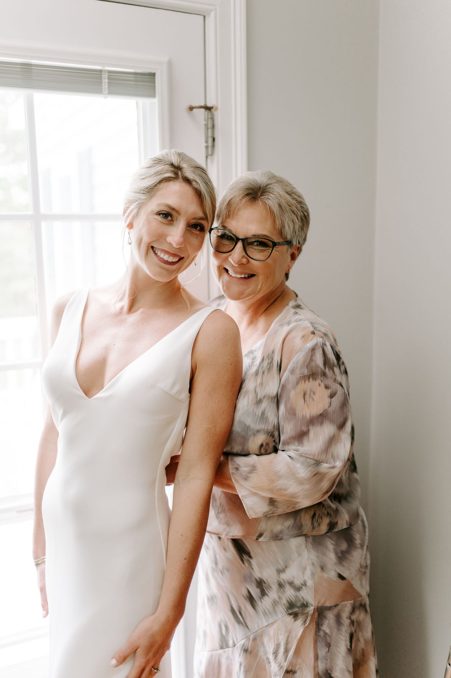 Two people embrace and laugh together in a bright room with white walls and windows.