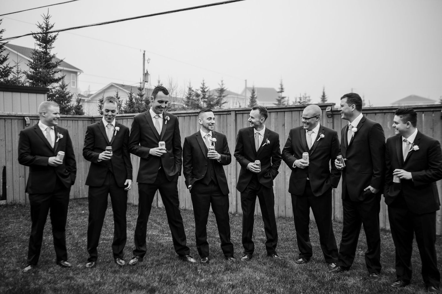A group of groomsmen in black suits and ties pose together outdoors in black and white.