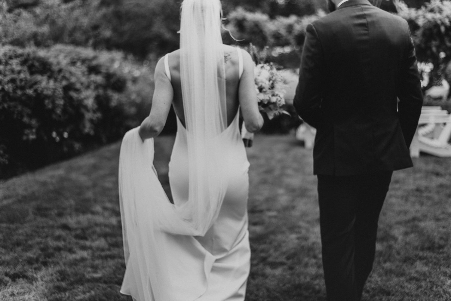 A dramatic black and white wedding photo showing flowing veil and elegant dress from behind.
