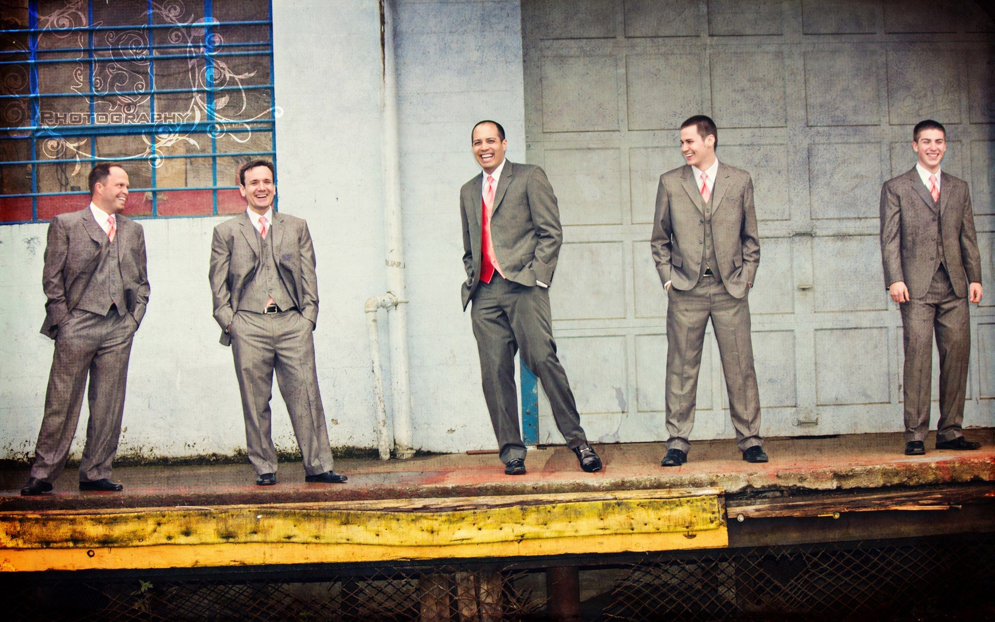 Groomsmen lined up against an industrial backdrop wearing matching gray suits.