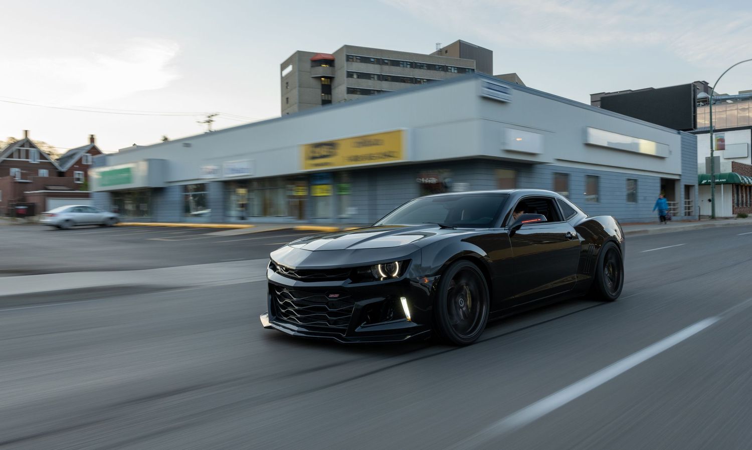 A murdered-out Chevrolet Camaro cruising through city streets at dusk.