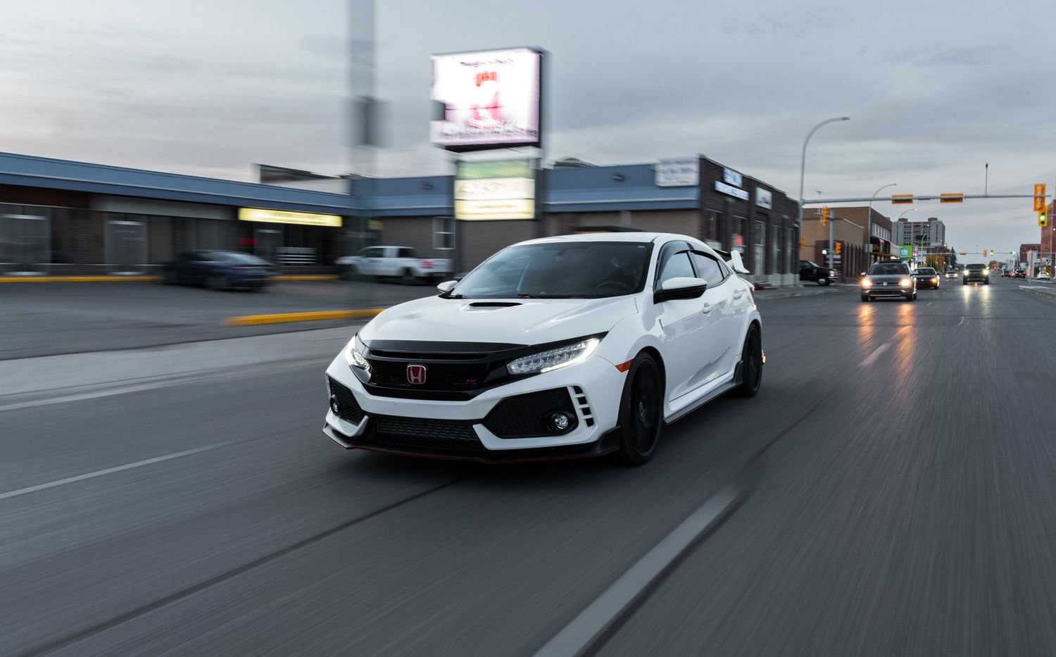 White Honda Civic Type R in motion on a city street during overcast weather.