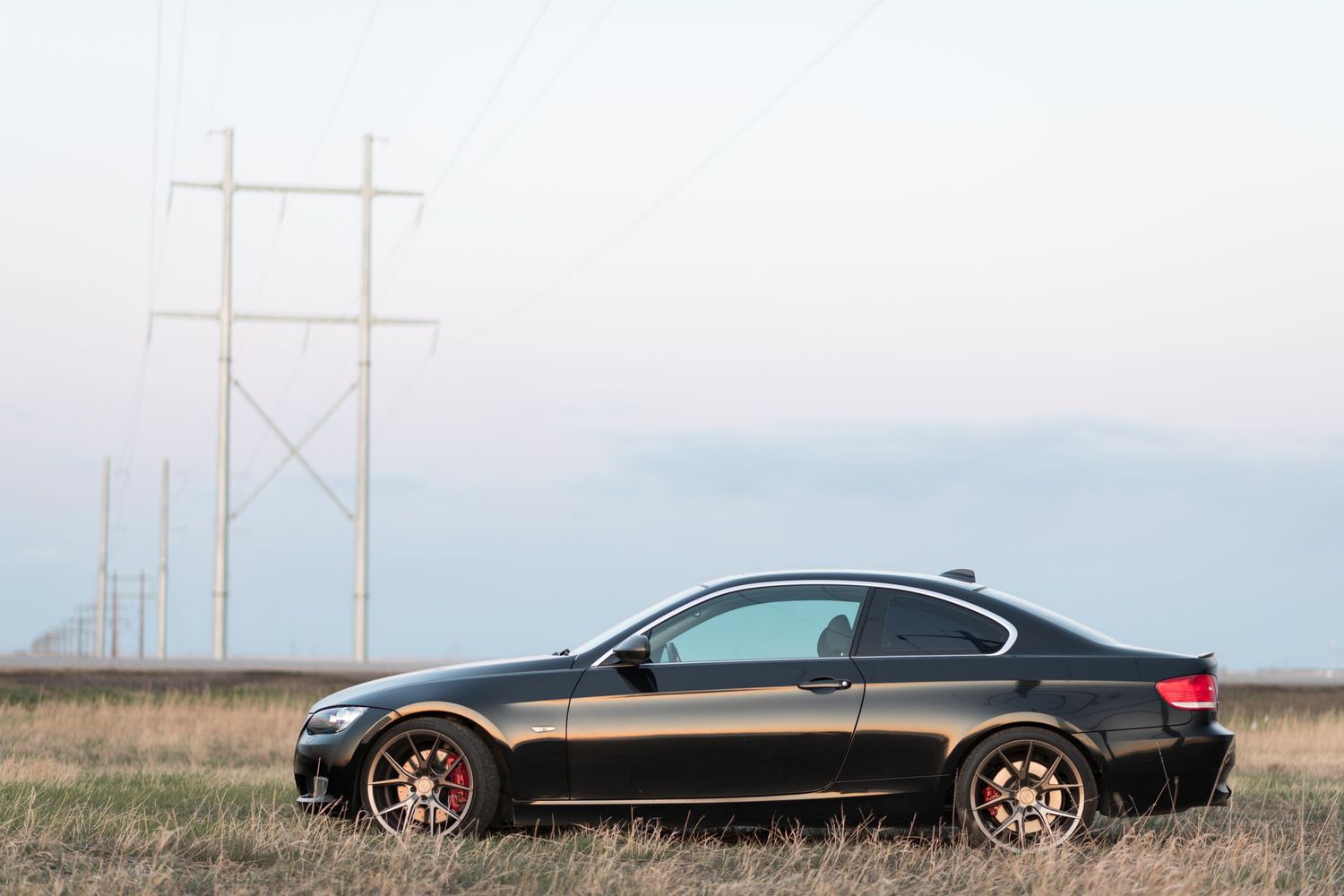 Black BMW sedan parked in an open field with power lines visible in the background.