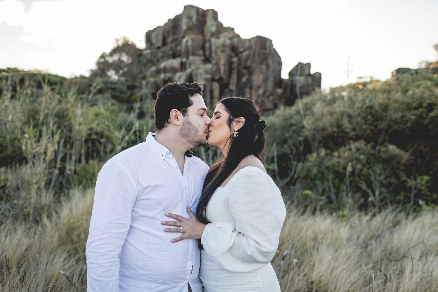 A couple shares an intimate moment in front of dramatic rock formations and wild grass.