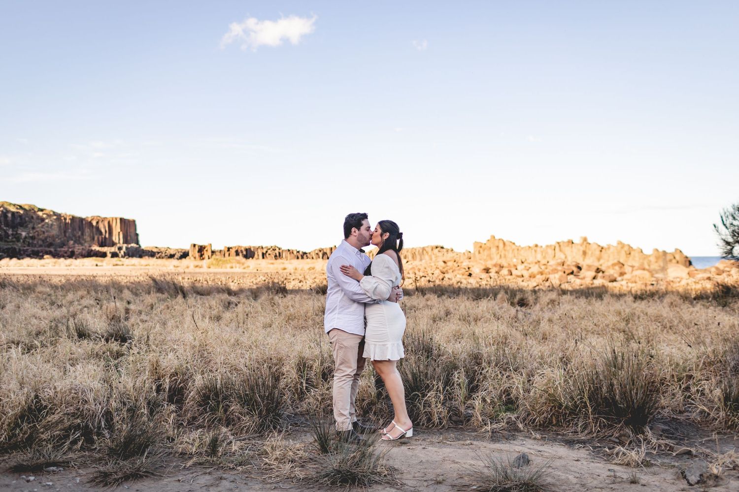 A loving couple stands together in an arid landscape with red rock formations in the background.