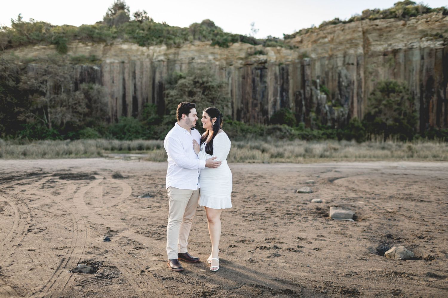 A couple poses together against dramatic vertical cliff formations in a desert setting.