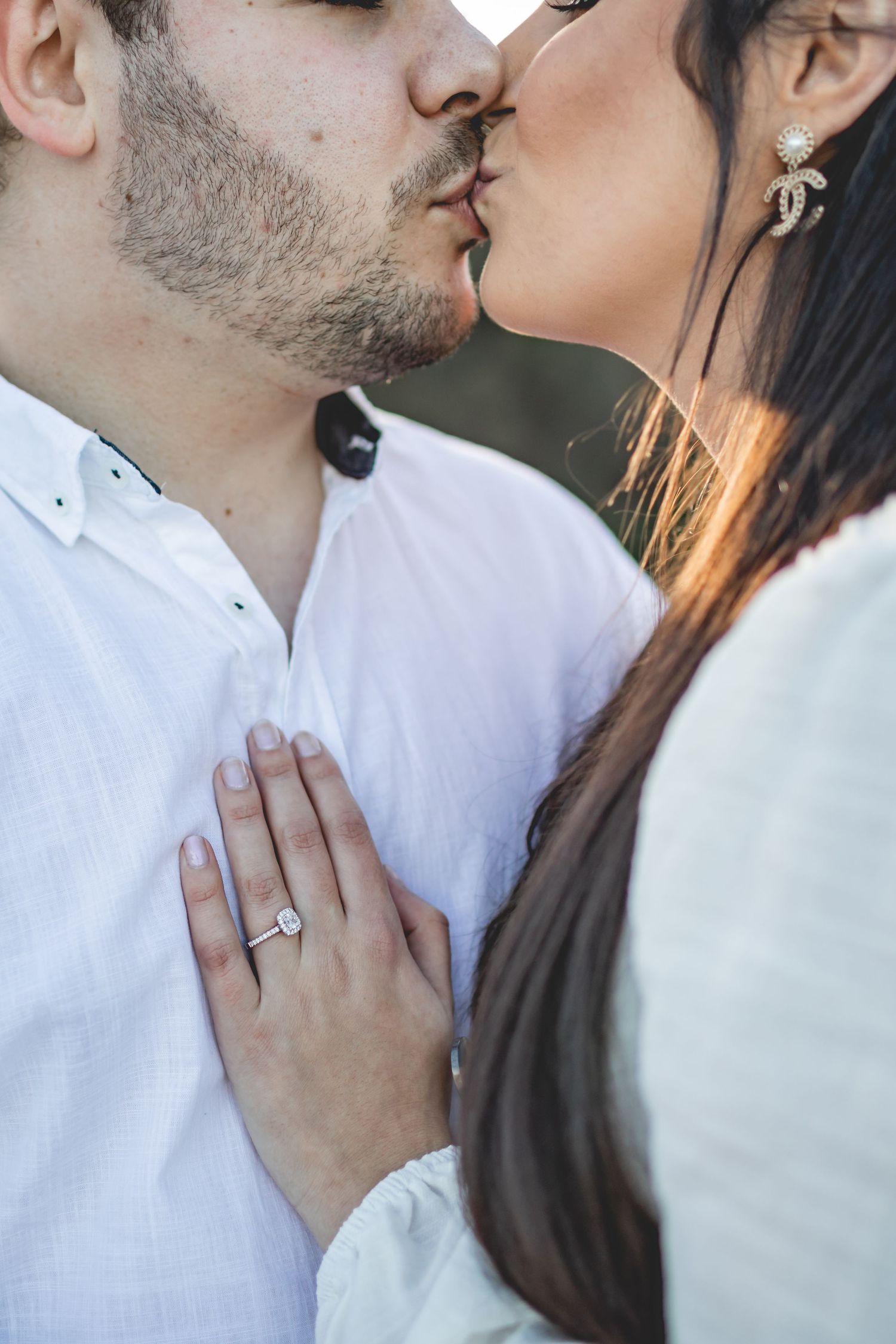 A close-up of an engagement ring while a couple shares an intimate kiss.