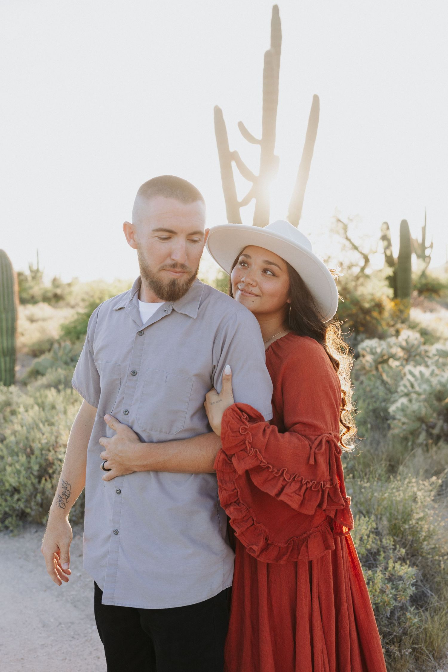 Romantic desert photoshoot with couple embracing among saguaro cacti at golden hour.