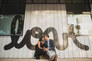 A couple sits beneath large decorative love typography on a wall.