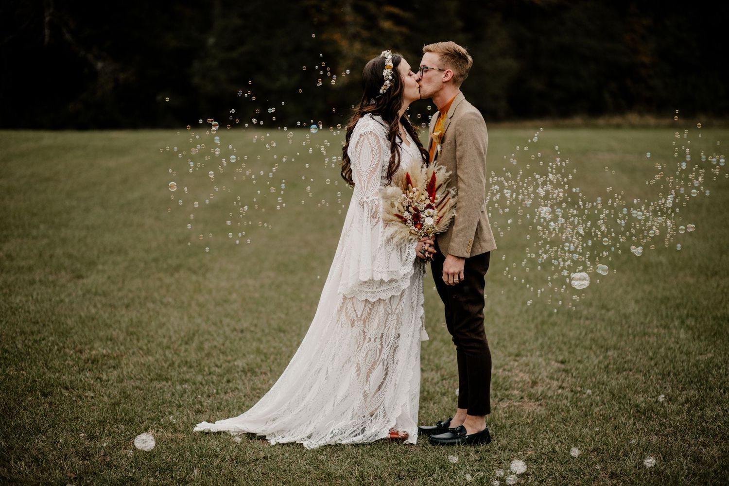 Couple in wedding attire surrounded by floating bubbles in outdoor garden setting.