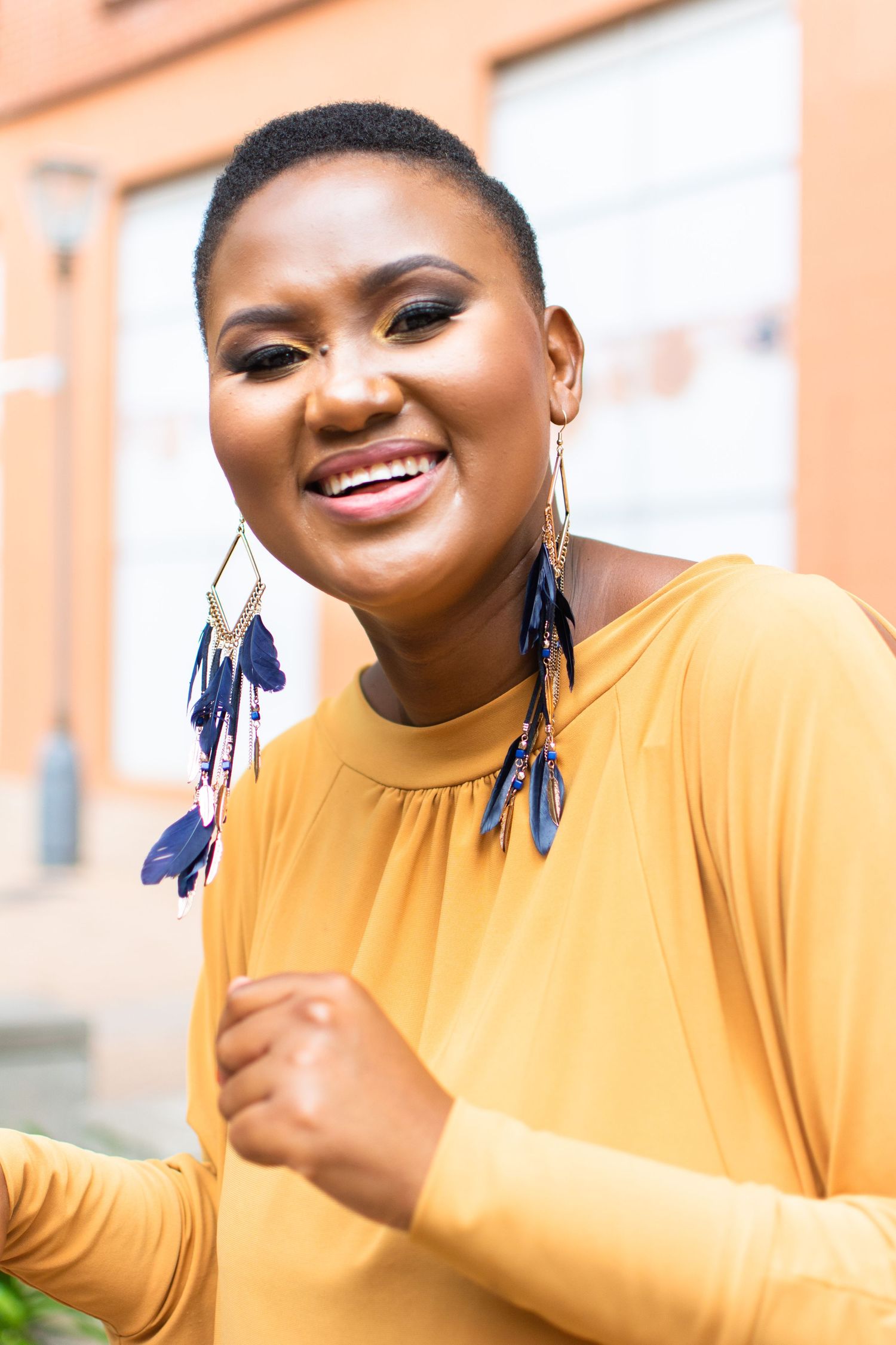 Woman in yellow top wearing statement tassel earrings against orange wall.