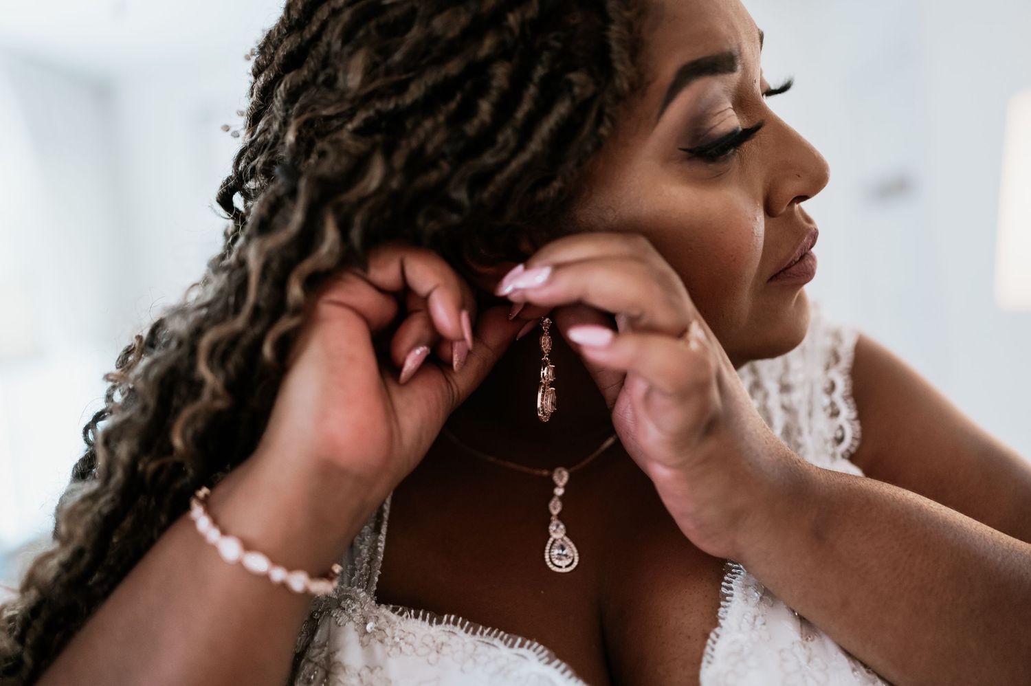 Close-up shot of hands fastening elegant diamond drop earrings on wedding day.