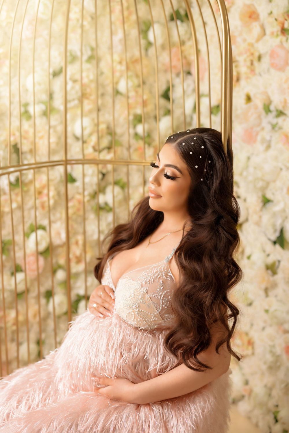 Dreamy maternity portrait in pink feathered gown beside ornate gold birdcage.