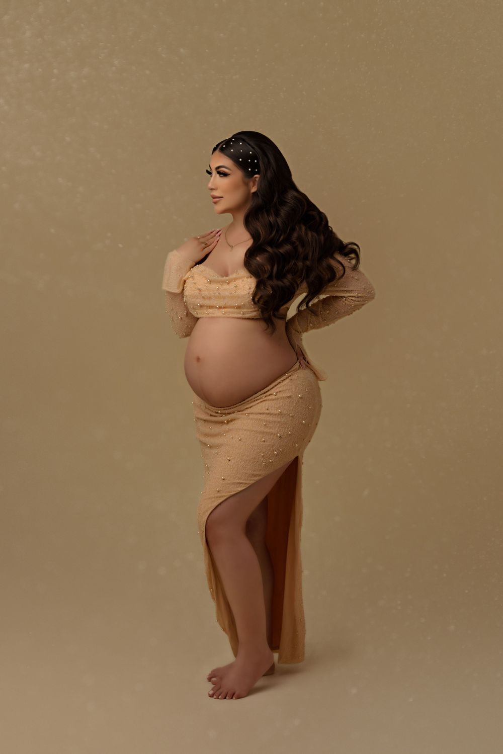 An elegant maternity portrait in golden tones with flowing fabric and romantic styling.