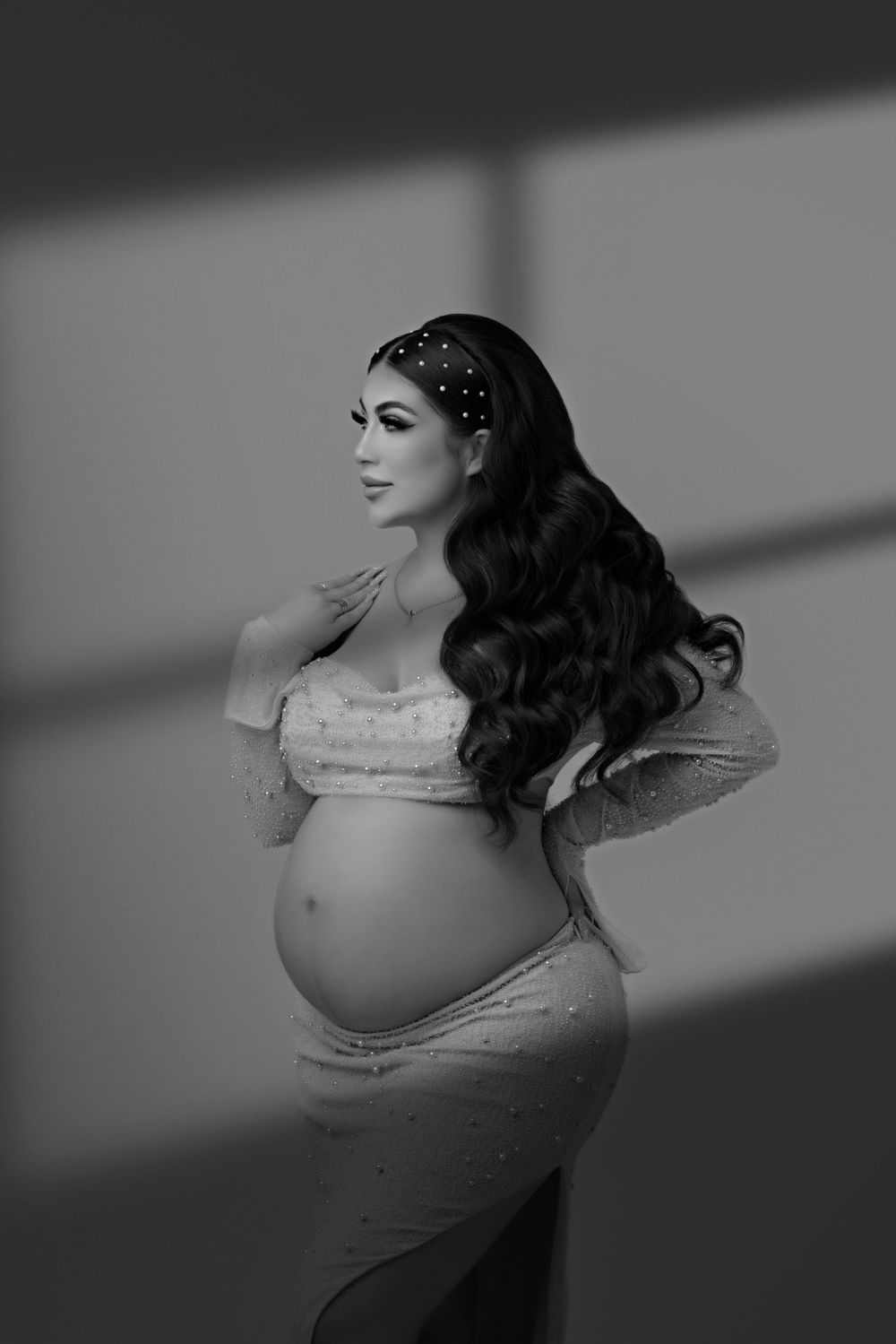 A black and white maternity portrait with dramatic lighting and vintage styling.