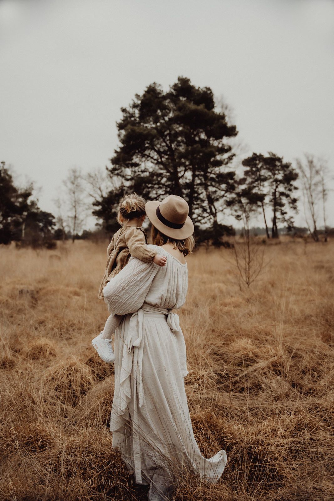A dreamy portrait in a sepia-toned field with tall pine trees in the background.