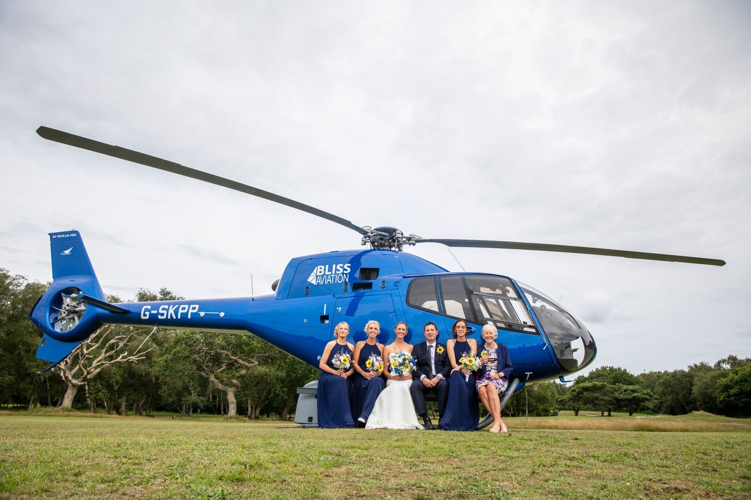 Blue helicopter parked on grassy field during a wedding event.