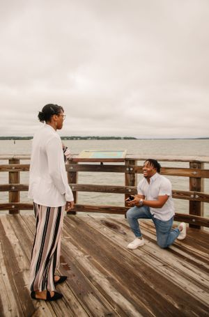 Surprise proposal moment on wooden pier overlooking water.