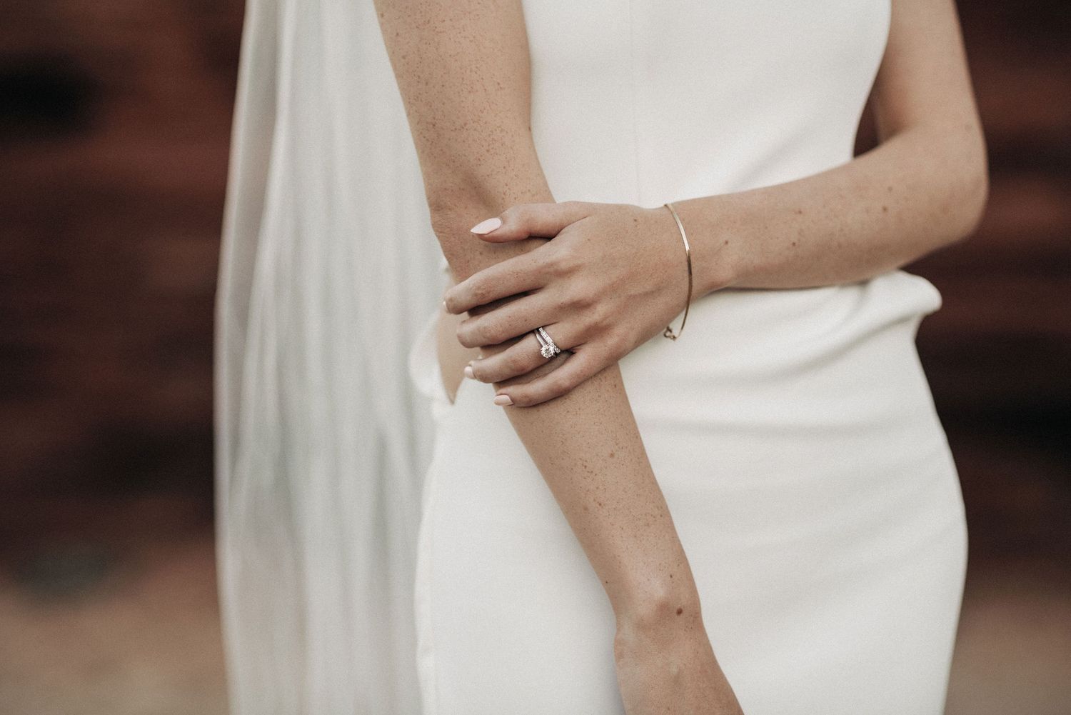Close-up of bride's hand with delicate bracelet against white wedding dress.