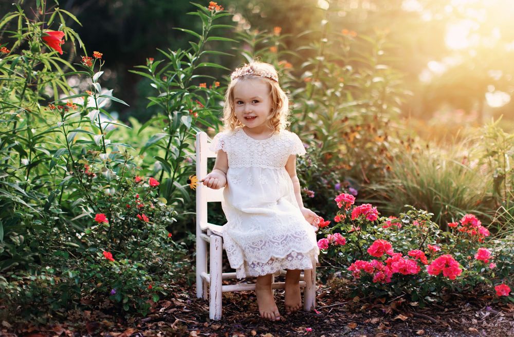 White lace dress portrait in garden with pink flowers and vintage chair.