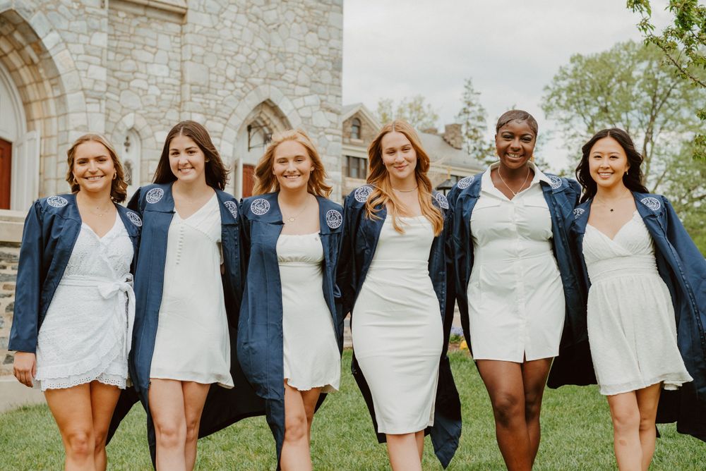 Villanova graduates in robes smiling in front of St. Thomas of Villanova Church