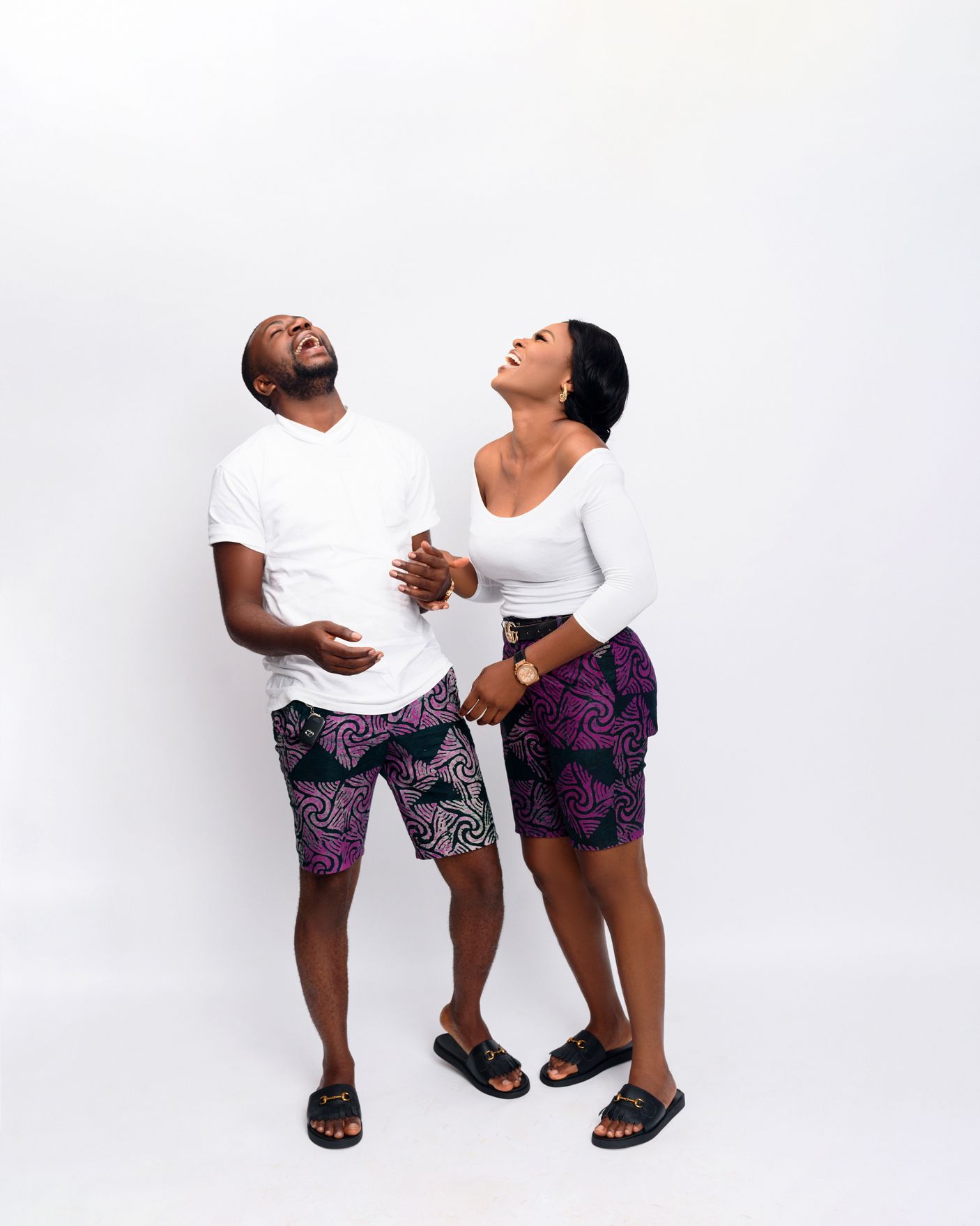 Couple wearing matching purple print shorts laughing together against white background.