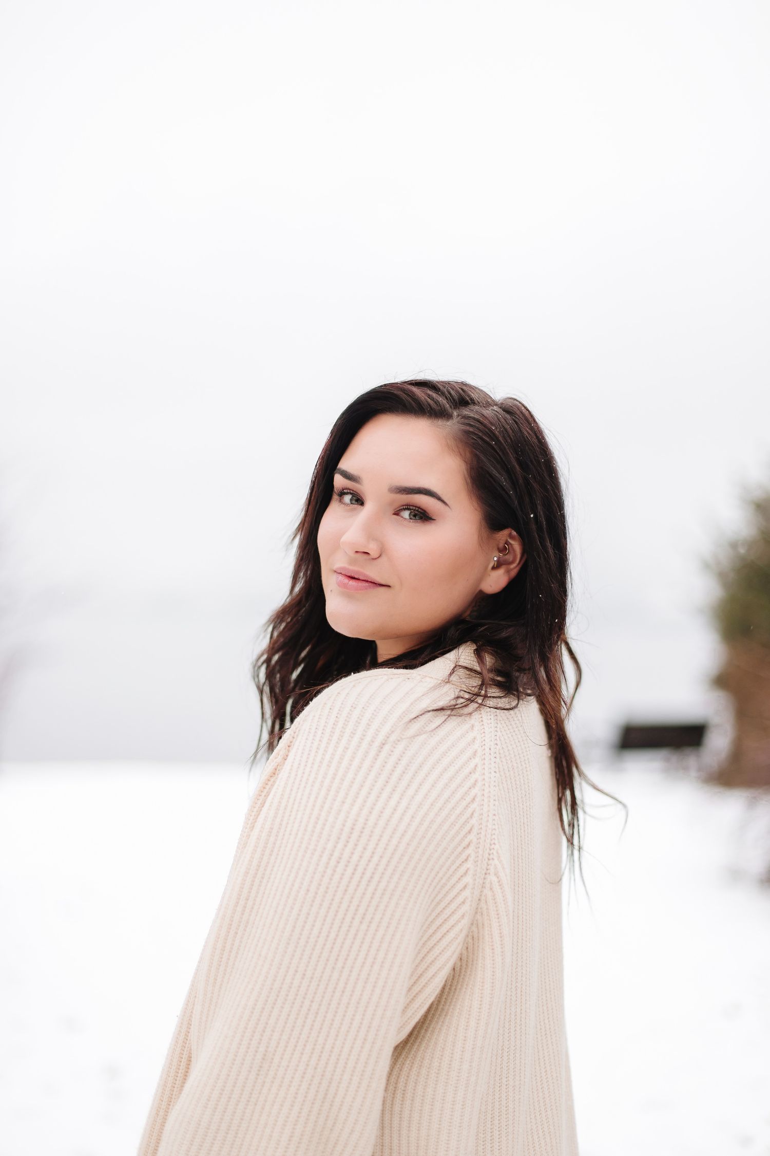 Soft winter portrait against white snowy background wearing a cozy cream ribbed sweater.