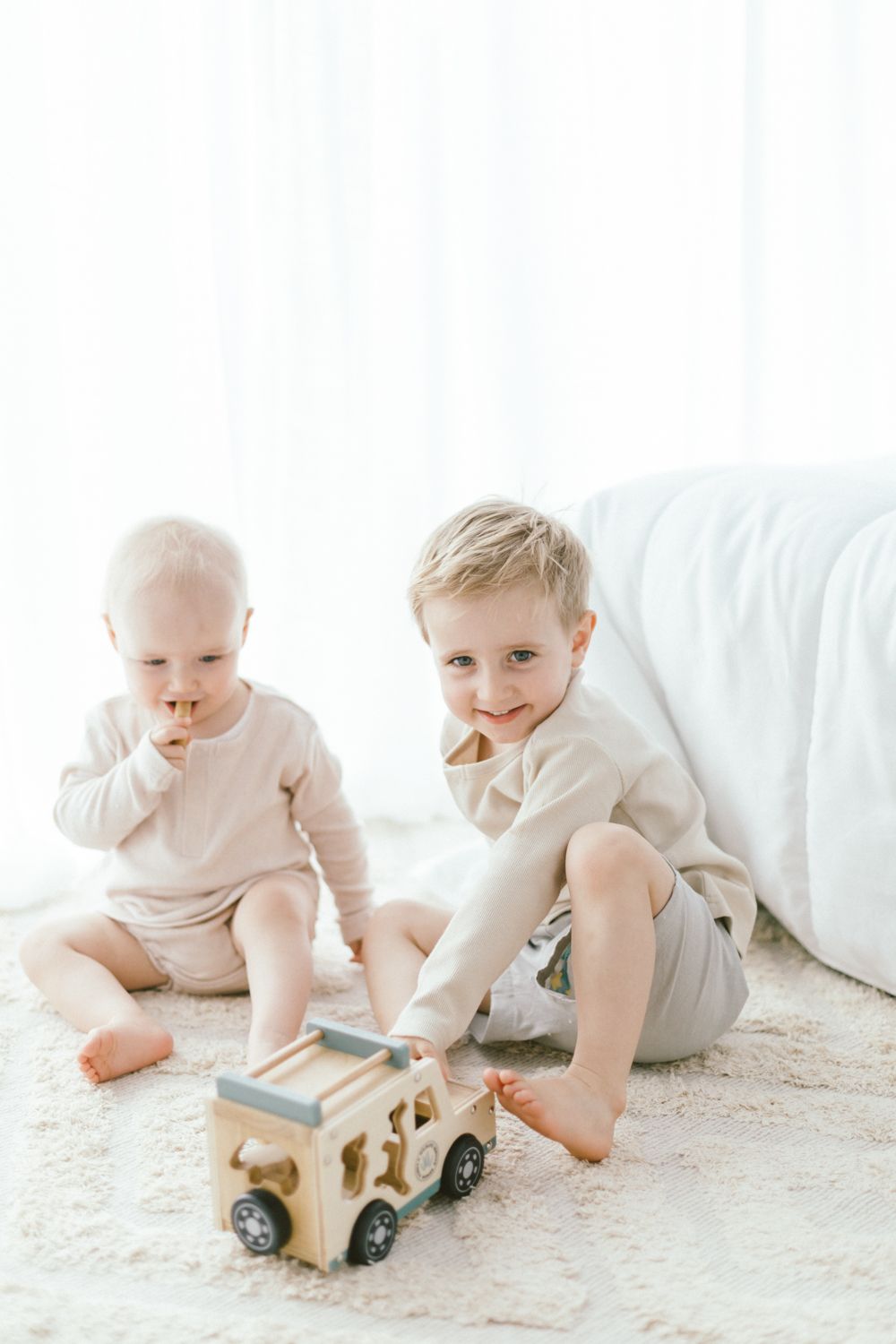 Baby plays with wooden toy train on white carpet in serene setting.