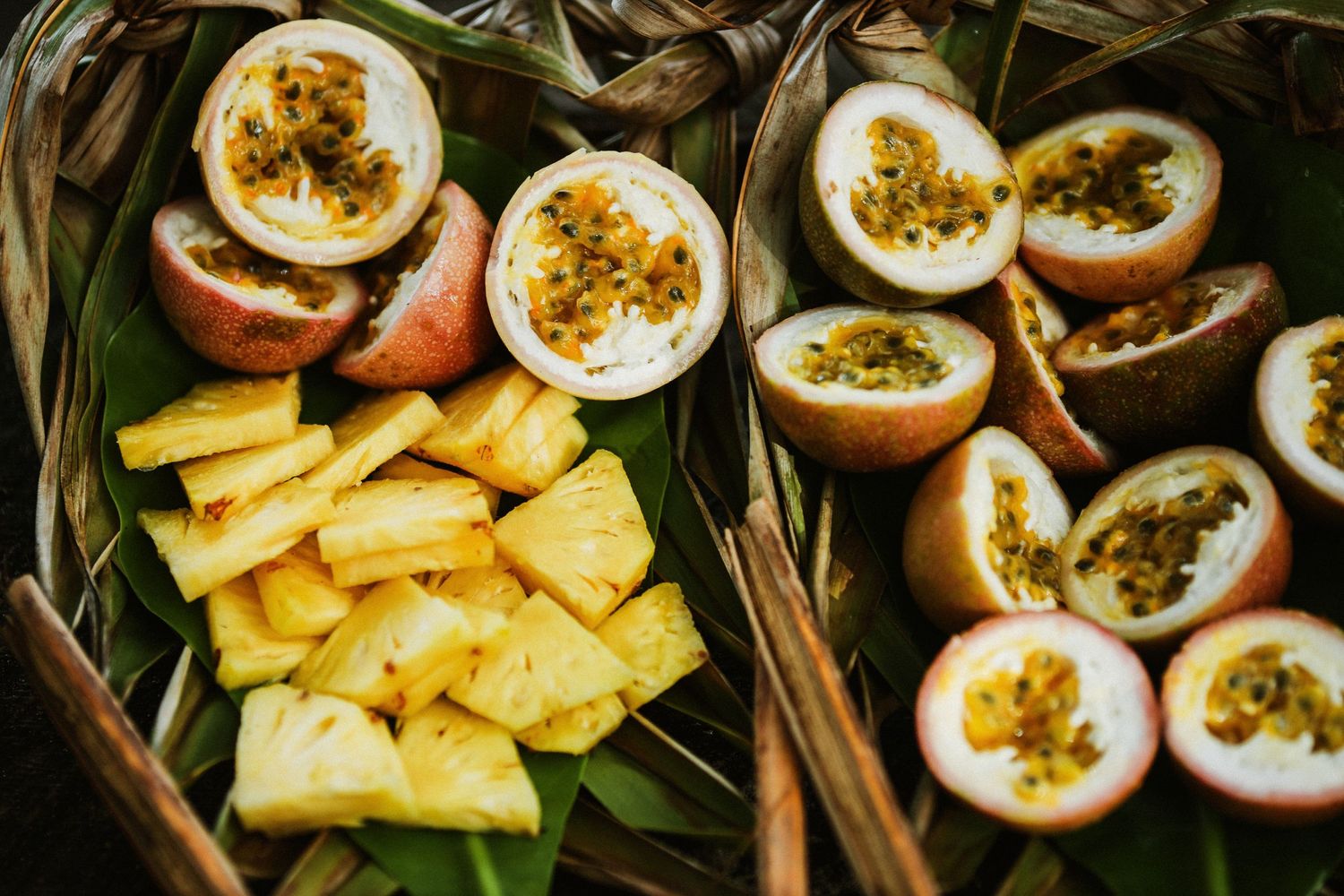 Fresh passion fruit and pineapple slices arranged in woven baskets with green leaves.