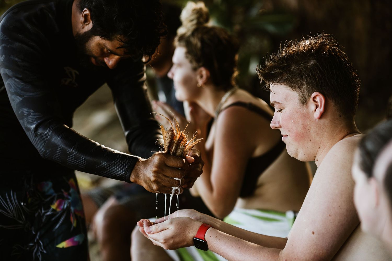 Beach gathering with people sharing drinks and snacks under palm trees.