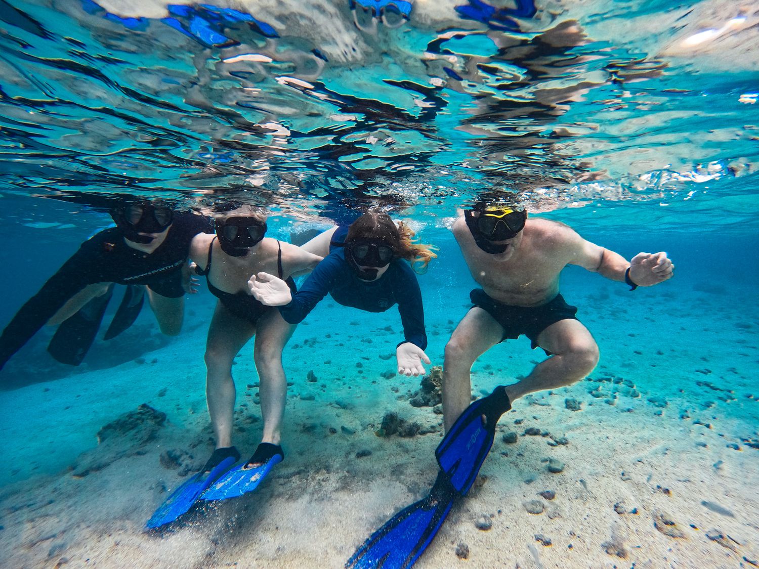 Snorkelers swimming in shallow crystal clear turquoise waters over sandy bottom.