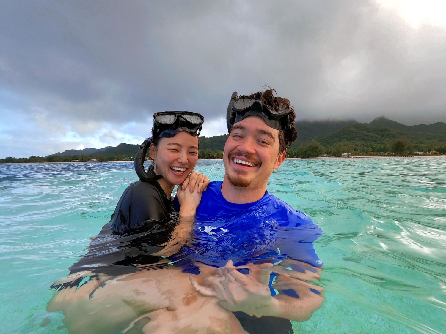 Two snorkelers enjoying tropical waters with mountains visible in background.